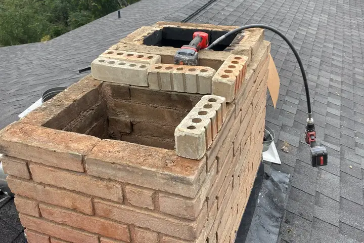 Brick chimney repair and masonry rebuild in progress on a Dallas roof